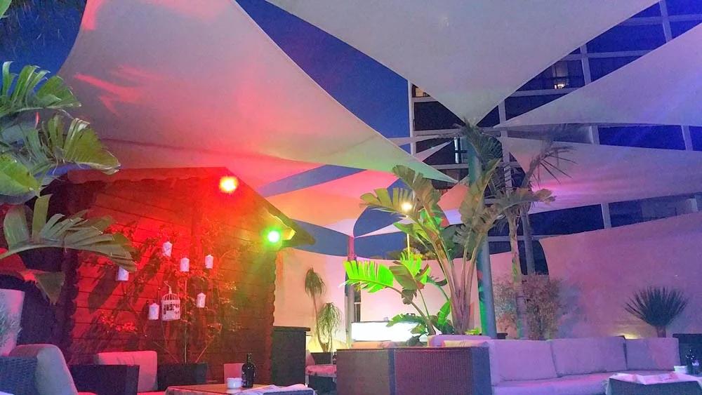 Layered commercial shade sails above an illuminated lounge terrace at night