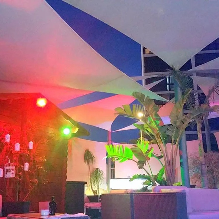 Layered commercial shade sails above an illuminated lounge terrace at night