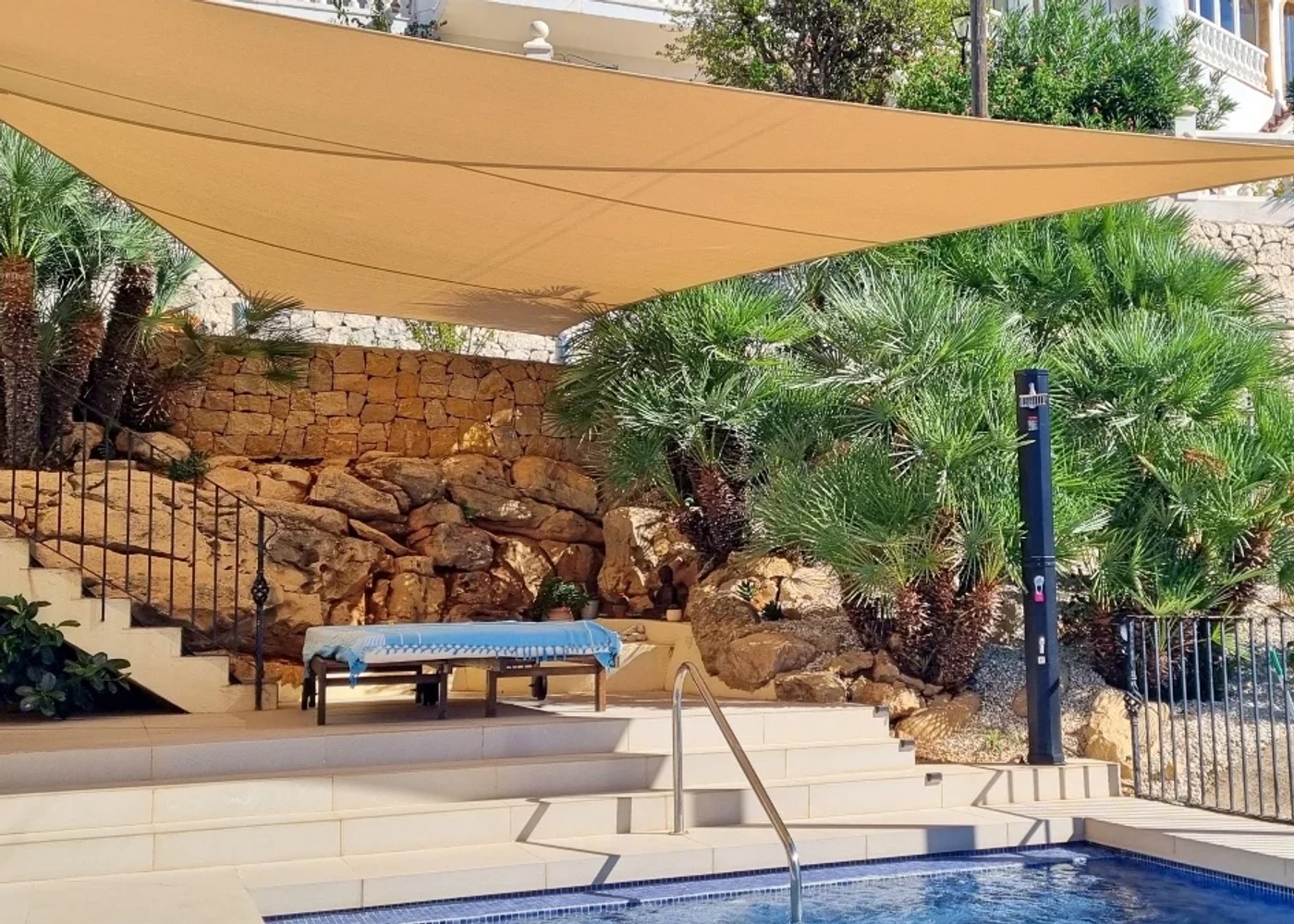 Maatwerk driehoekig schaduwdoek boven een poolterras met natuurstenen muren