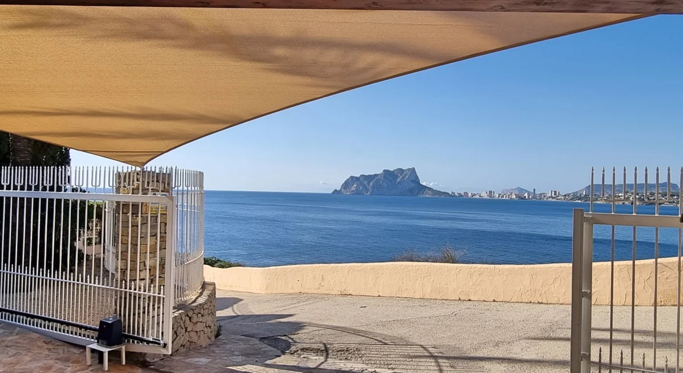 Schaduwdoek boven een terras met zeezicht en de Penon de Ifach op de achtergrond