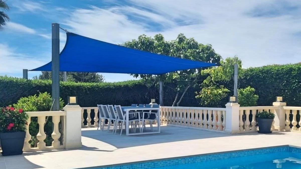 Blue triangular shade sail installed above a poolside terrace seating area
