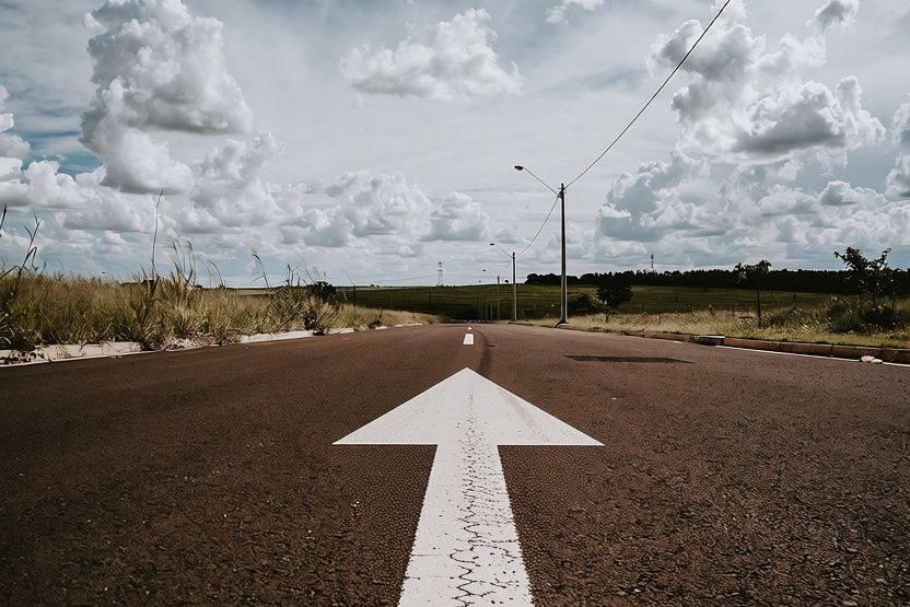 A white arrow painted on a dark road points forward under a dramatic cloudy sky.