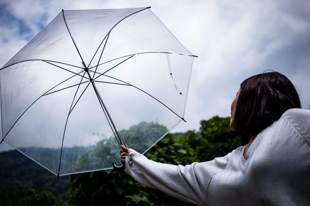 Person holding a clear umbrella, looking up at the cloudy sky.