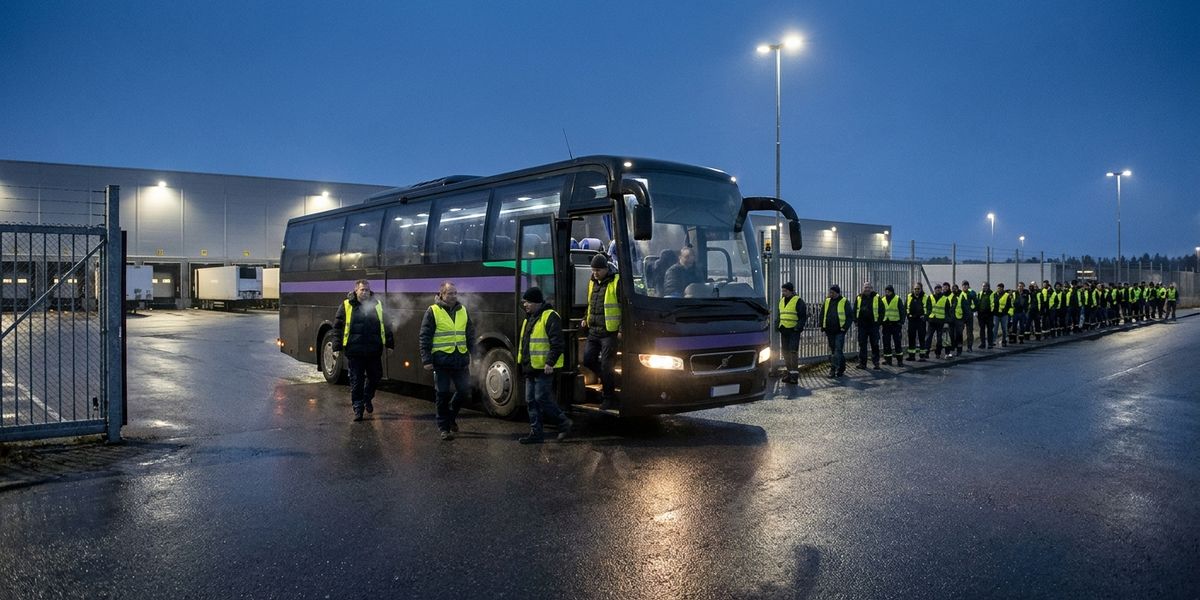 Saisonkräfte steigen vor Sonnenaufgang aus einem Shuttle am Tor eines Versandzentrums, dahinter eine lange Warteschlange