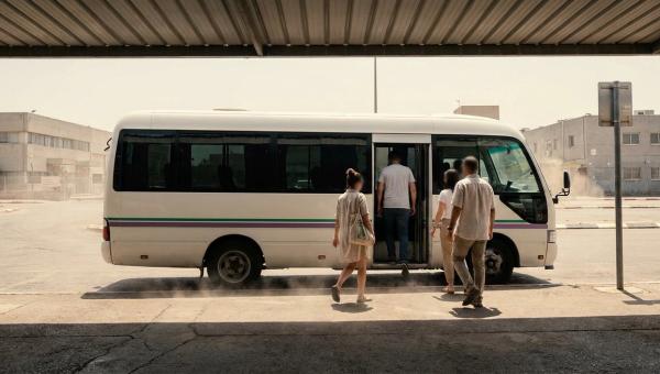 עובדים עולים להסעה ממוזגת בתחנת איסוף מוצלת בשרב ישראלי, על רקע אזור תעשייה ואדוות חום מהאספלט