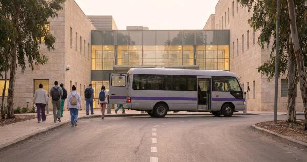 מיניבוס הסעות משמרות מוריד צוות רפואי בכניסת העובדים של בית חולים לפנות בוקר.