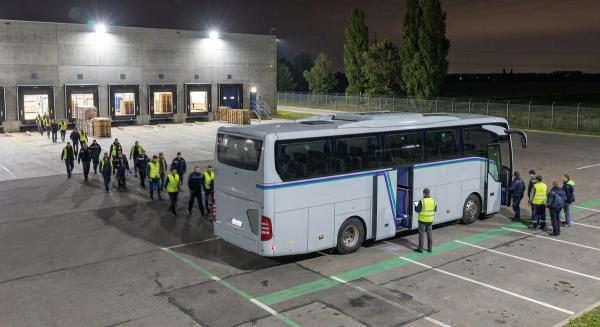 Нічна пересменка біля розподільчого центру за містом: працівники сідають у службовий автобус під освітленими доками