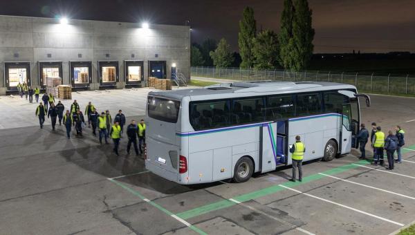 Нічна пересменка біля розподільчого центру за містом: працівники сідають у службовий автобус під освітленими доками