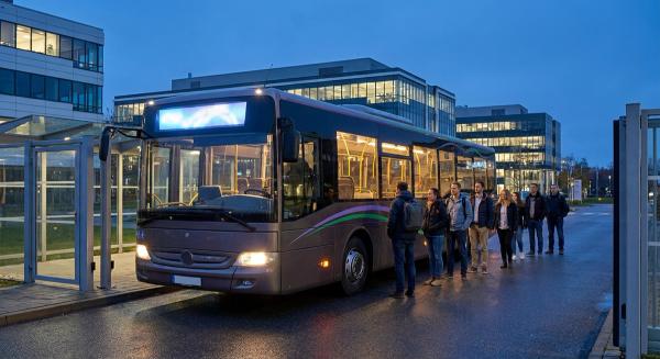 Корпоративний шатл чекає біля прохідної промислового обʼєкта ввечері, поки працівники спокійно заходять у салон.