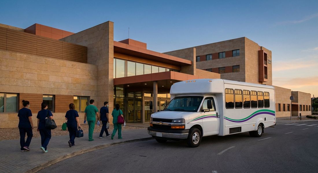 Autobús lanzadera frente a la entrada de un hospital español al anochecer, durante un cambio de turno