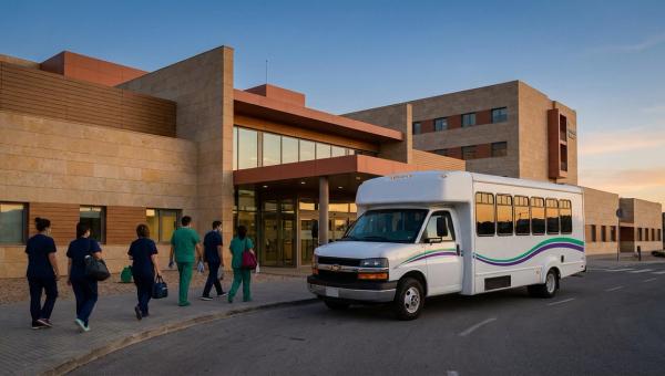 Autobús lanzadera frente a la entrada de un hospital español al anochecer, durante un cambio de turno