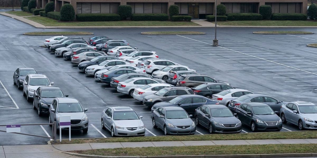 Suburban corporate parking lot full at midday Tuesday with a queue of cars at the entrance, contrasted with empty stalls visible at the back