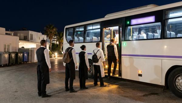 Personal de hotel con uniforme sube a una lanzadera de empresa en la entrada de servicio de un resort balear de madrugada.