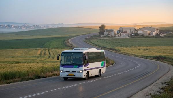 מיניבוס הסעה ארגוני נוסע בכביש כפרי לעבר אזור תעשייה בפריפריה בשעת בוקר מוקדמת, גבעות הגליל ברקע