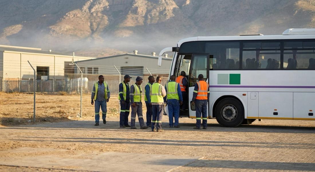 Operadores con chaleco reflejante abordan un camión de personal en la puerta de un parque industrial al amanecer en el norte de México