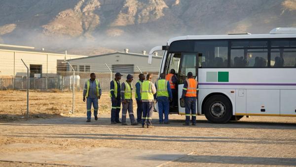 Operadores con chaleco reflejante abordan un camión de personal en la puerta de un parque industrial al amanecer en el norte de México