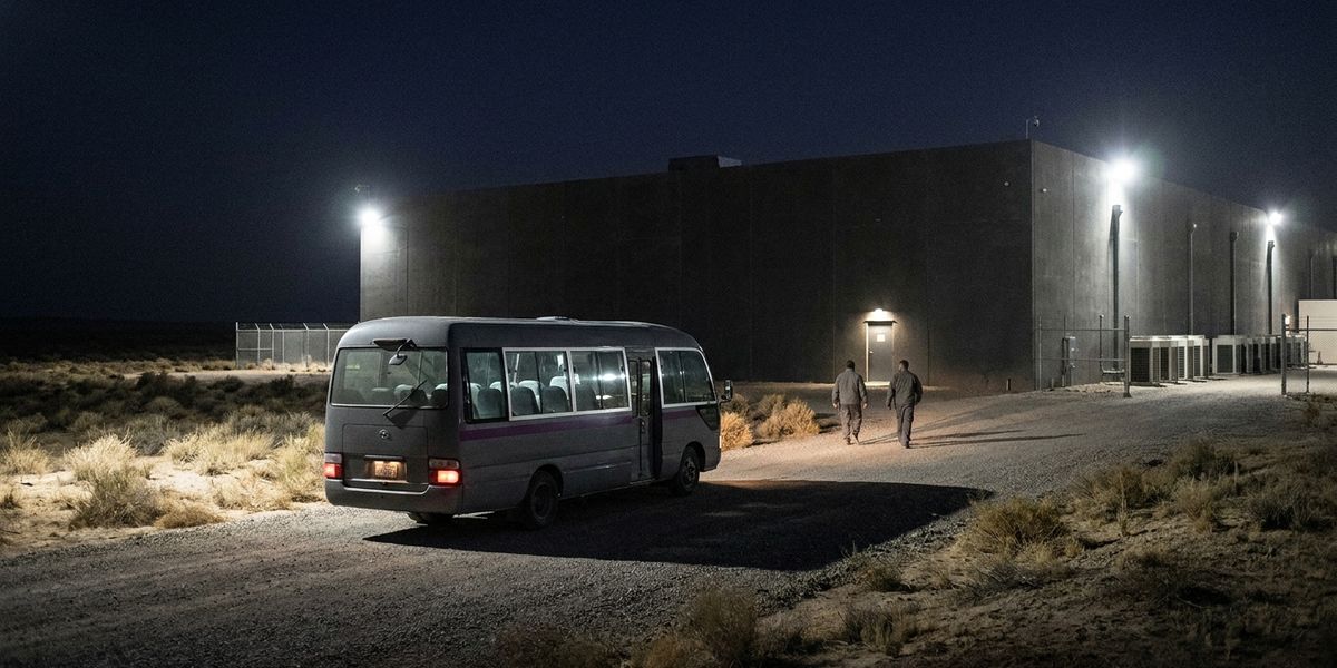 מיניבוס ממתין בלילה בדרך הגישה למרכז נתונים מבודד, שני טכנאים הולכים לעבר דלת כניסה מוארת