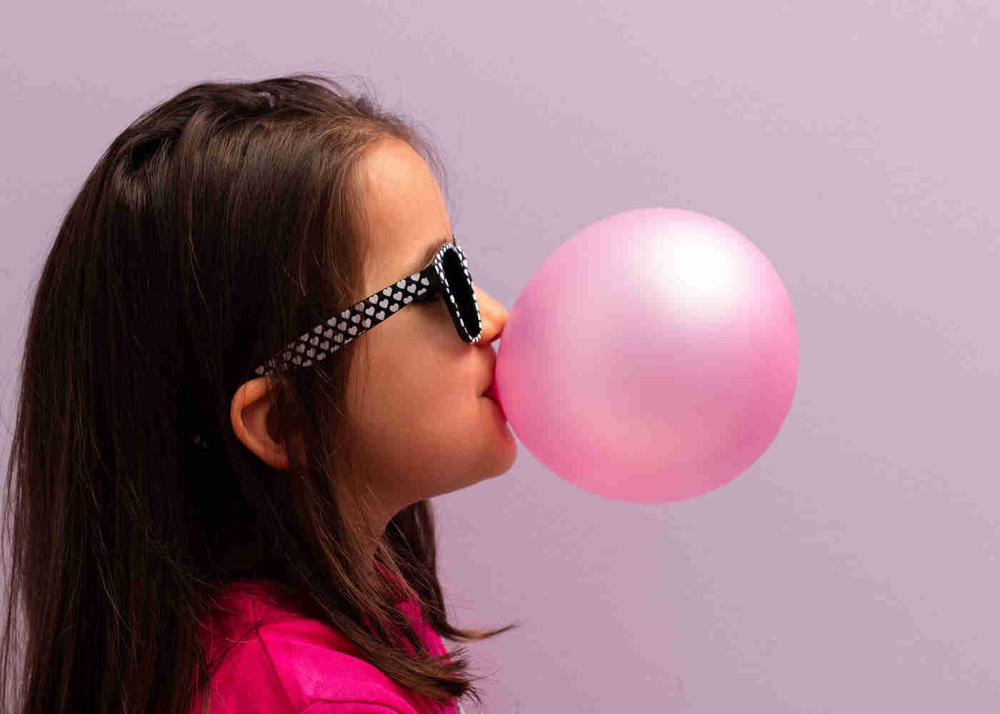 Pretty young girl with sunglasses on blowing a bubble gum bubble