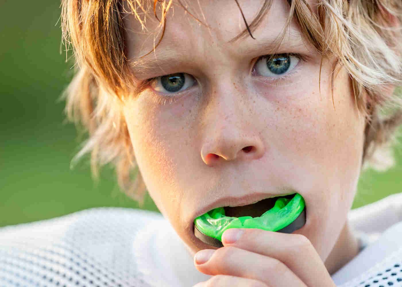 Teenage boy in football pads removes sports mouthguard
