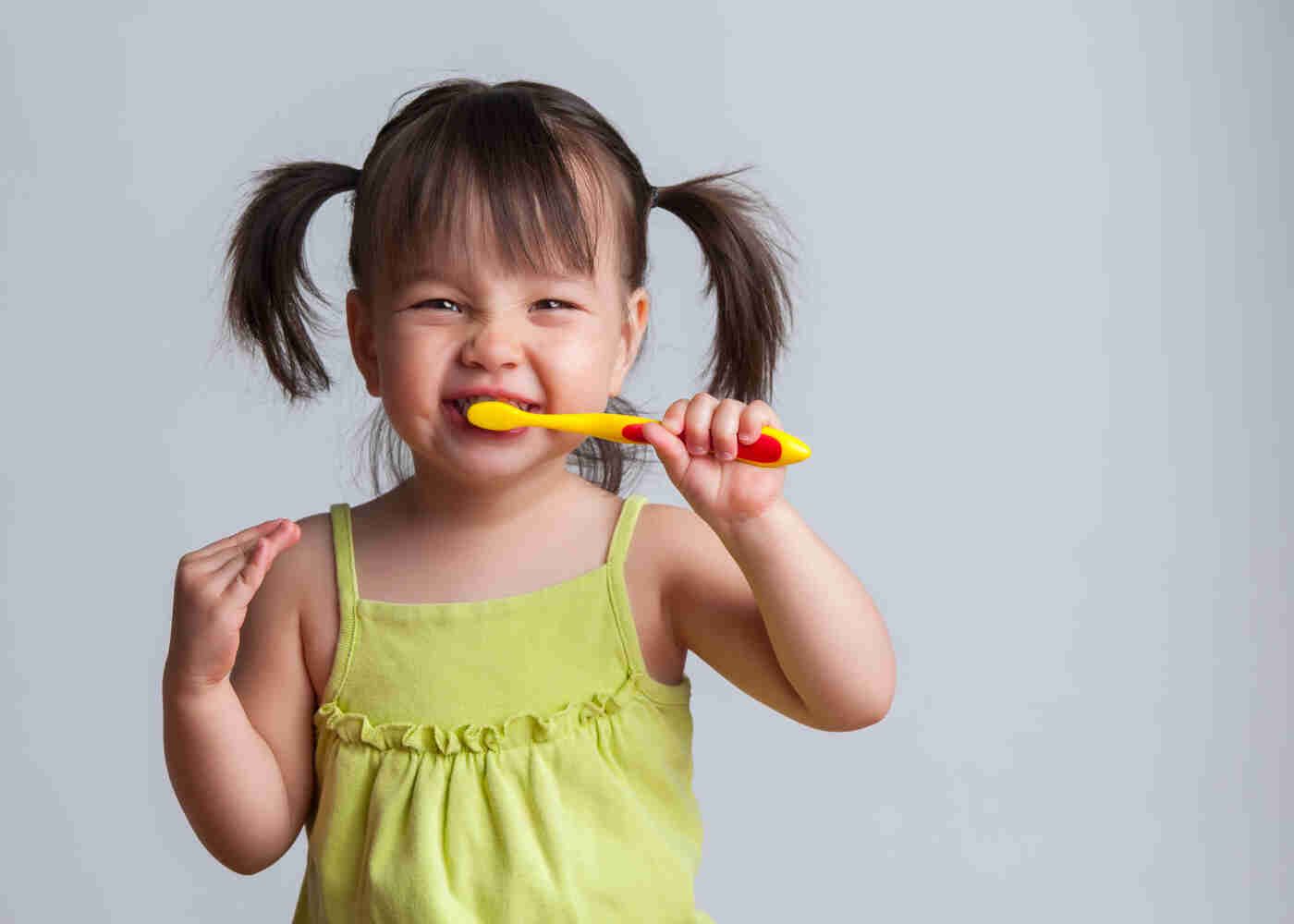 Cute little girl with ponytails is brushing her teeth