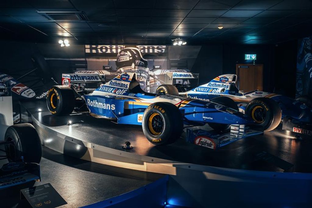 Two blue and white Rothmans Formula 1 race cars on display in a museum.
