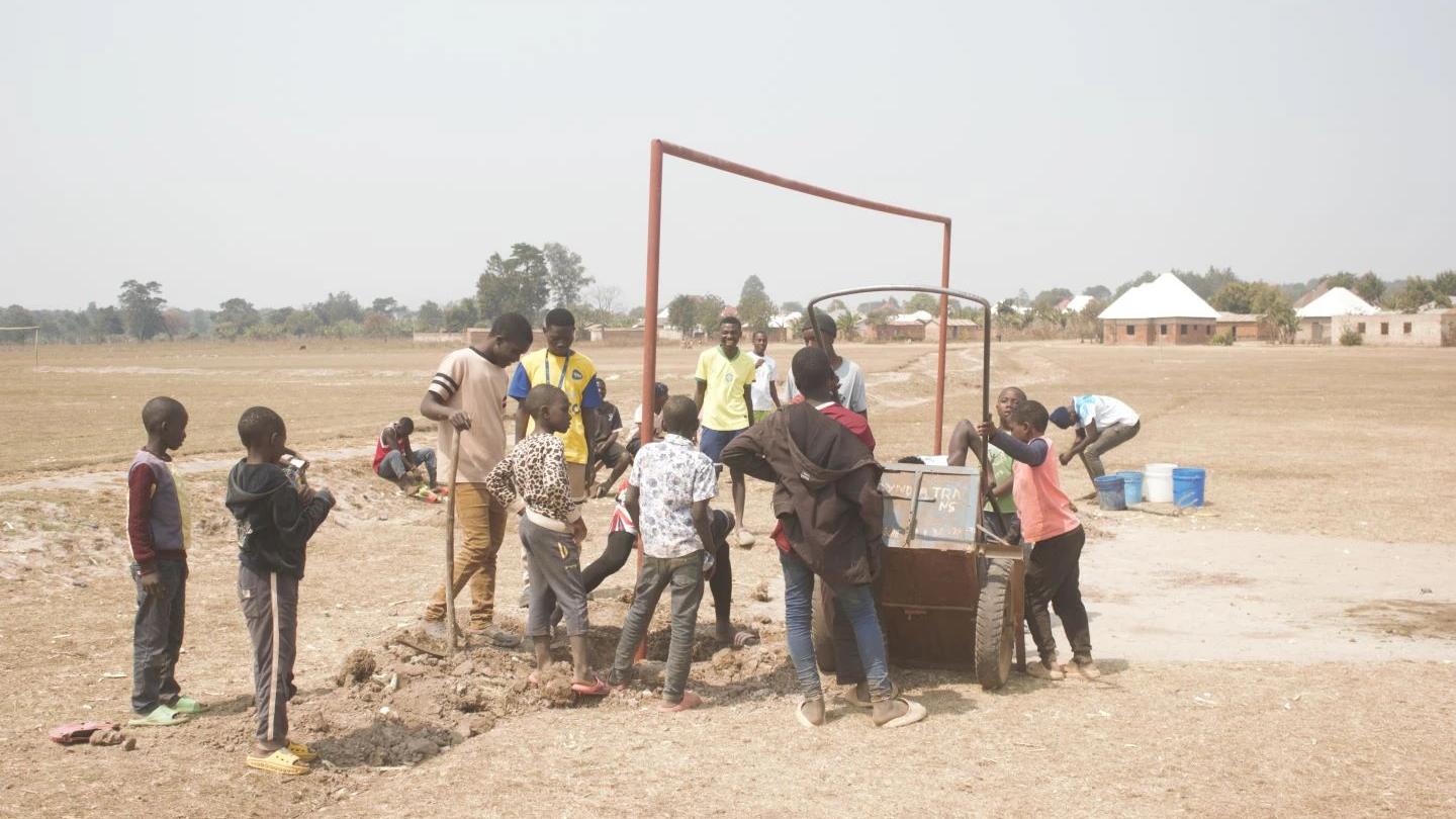 Young people and community members working together during the installation of a new steel football goal at the YOSSO field.