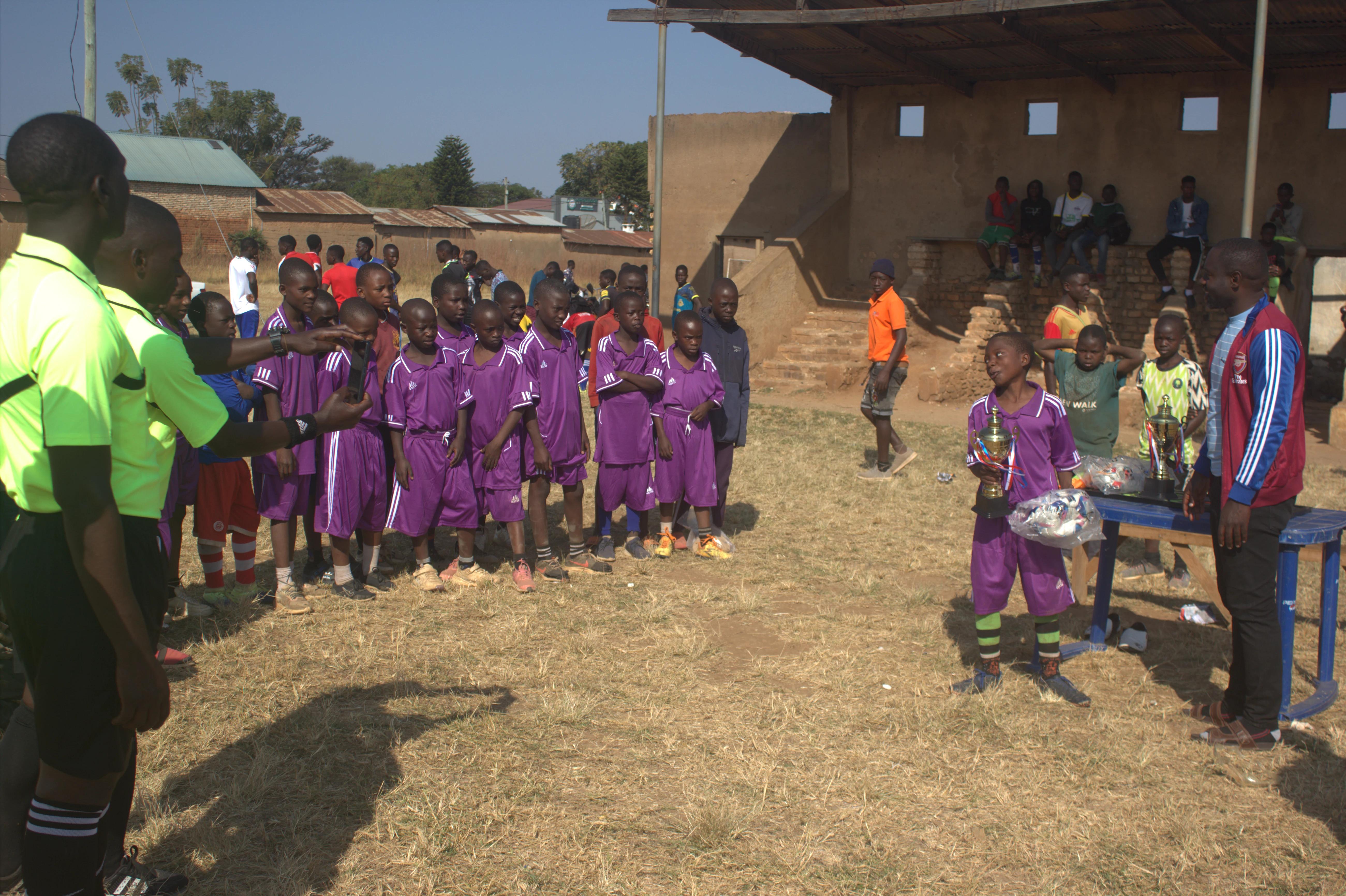 Referees and a purple-kitted team gathered as a player holds a trophy pitchside