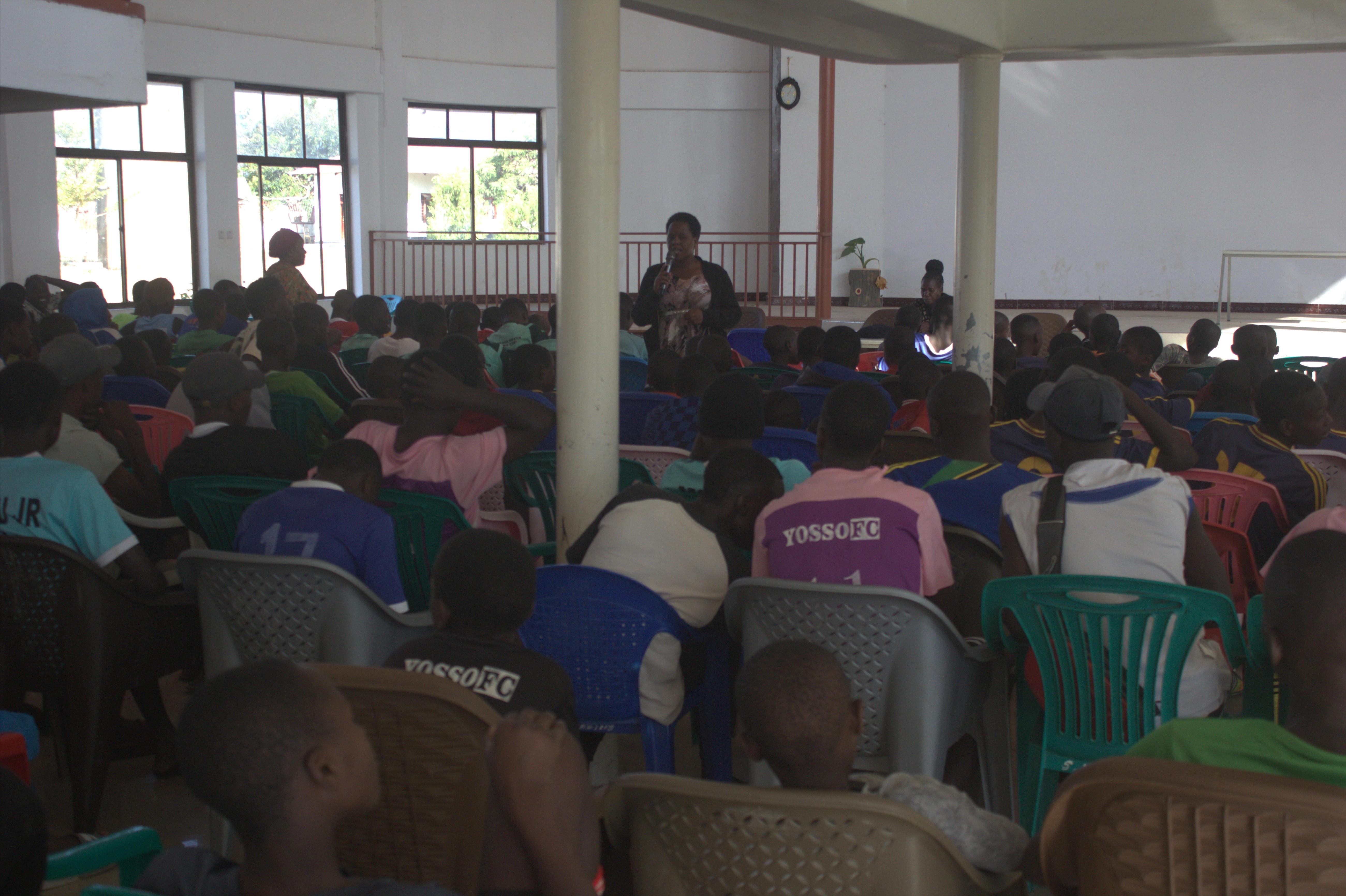 Organiser speaking into a microphone to seated teams indoors
