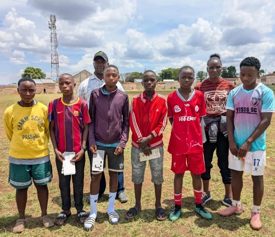 Young football players and coaches standing together on a football field following a player screening activity in Mbozi.