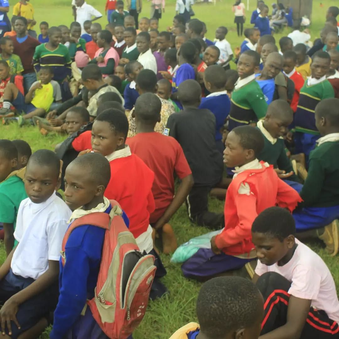 Large group of schoolchildren seated on grass at an outdoor gathering