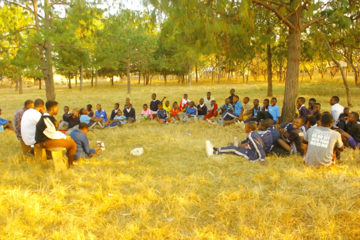 Children and youth sitting under trees during a group session