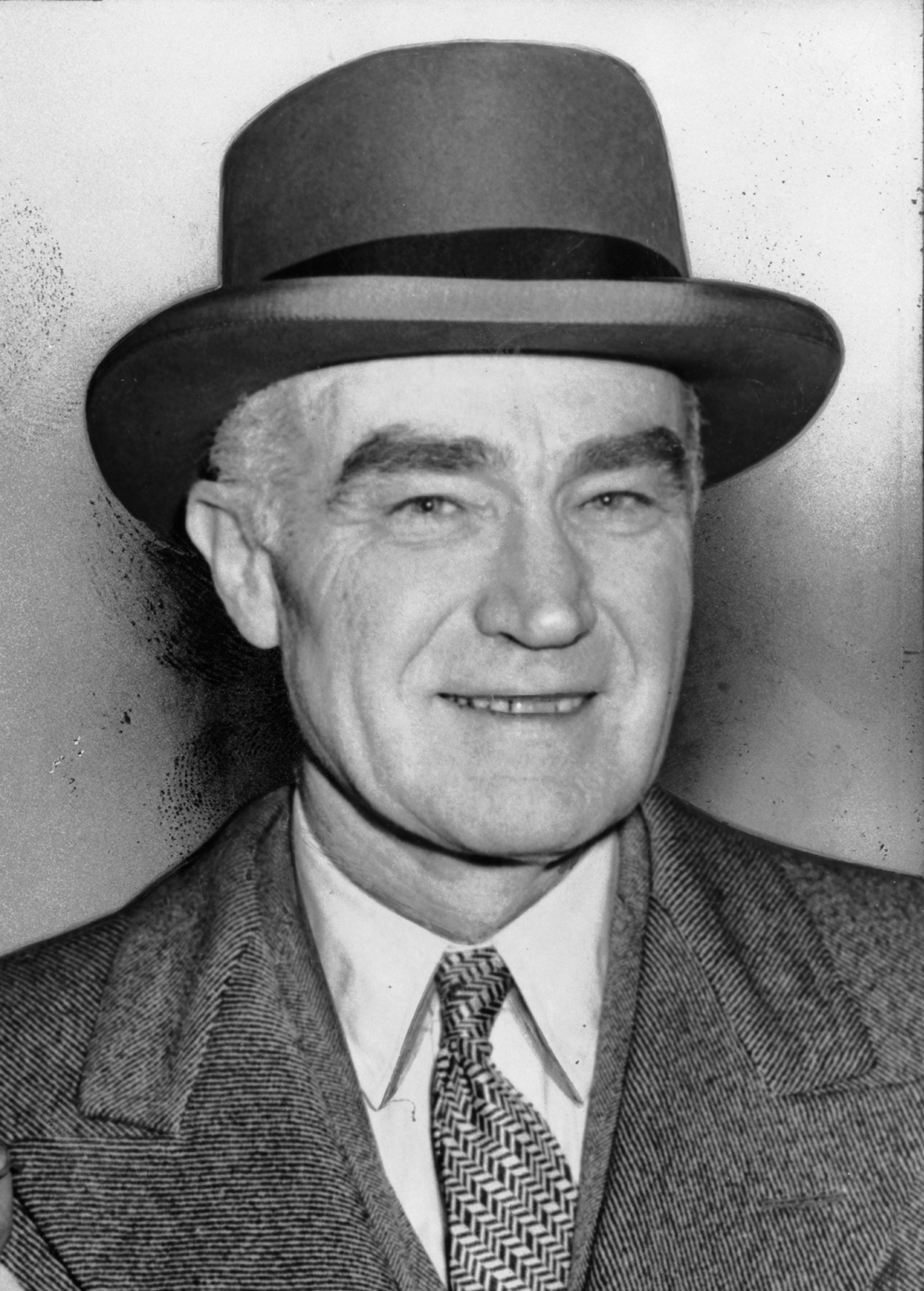 A Portrait of Henry Luce, an older white map wearing a top hat and a herringbone jacket with a white shirt and a patterned tie.