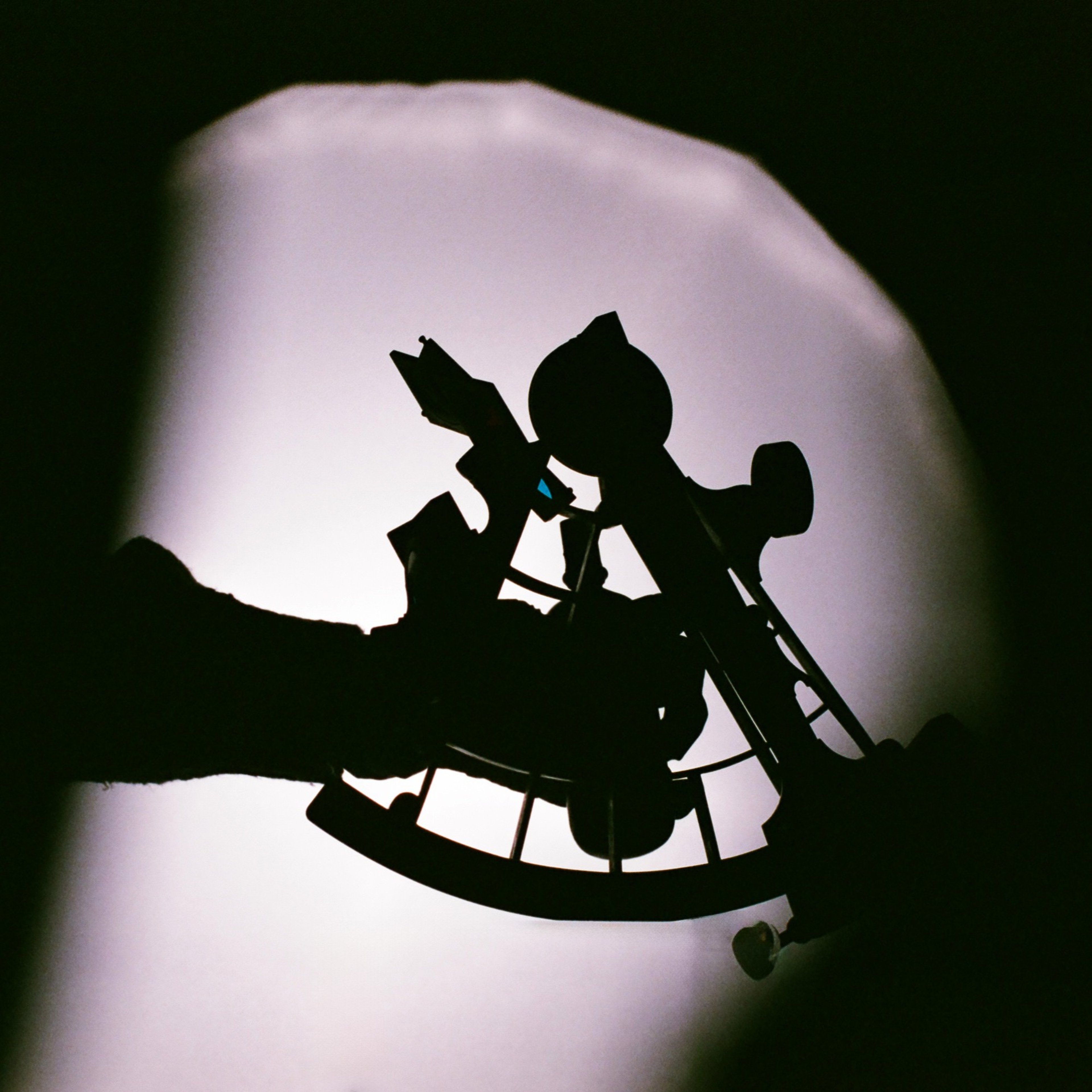 A silhouette of a hand holding a sextant - a historical device for celestial navigation - in front of a light