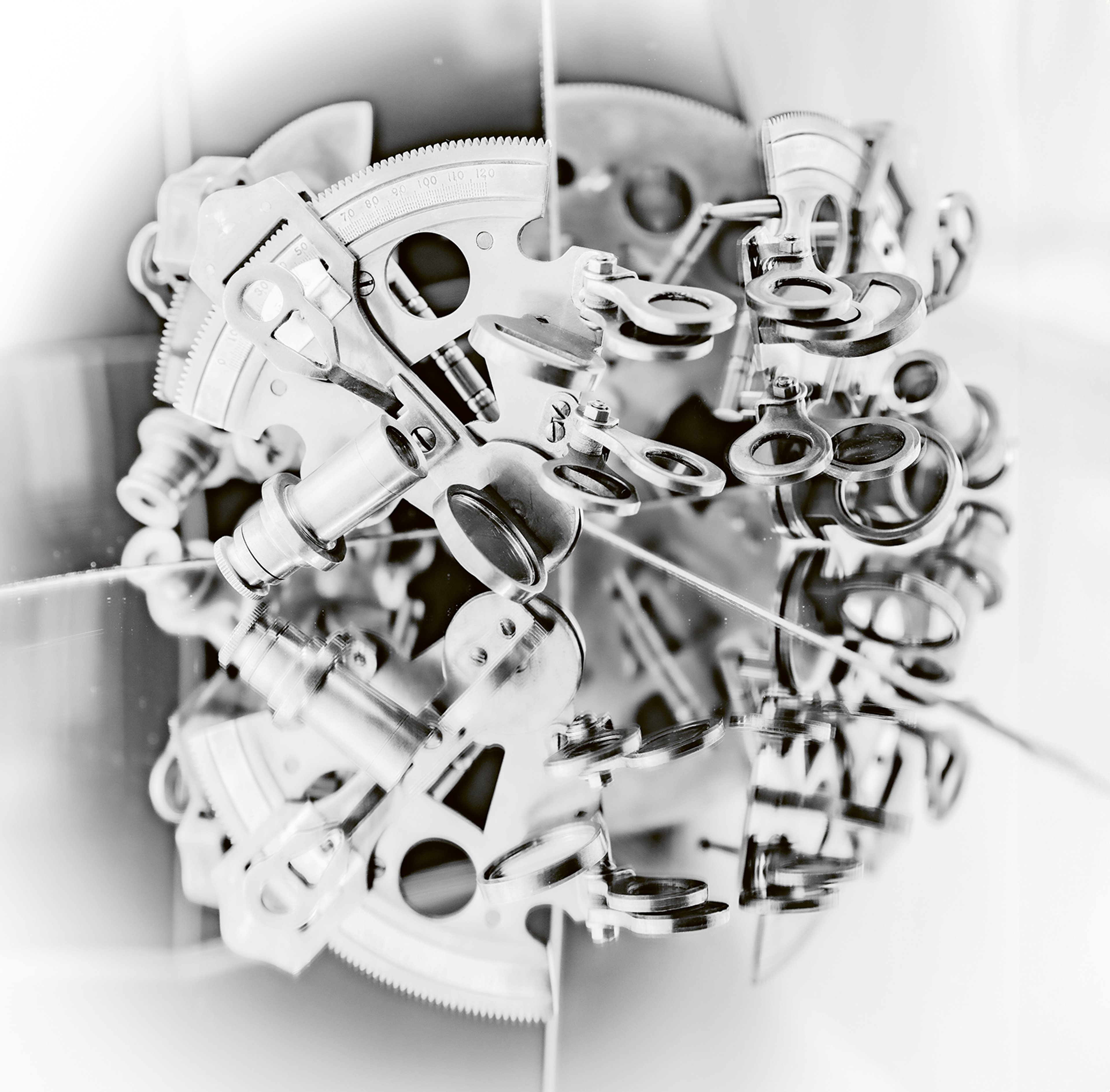A black and white photographic image showing a sextant - a scientific navigational instrument - which has been placed on top of a mirror so an almost-circular repeating image of the instrument has been created.