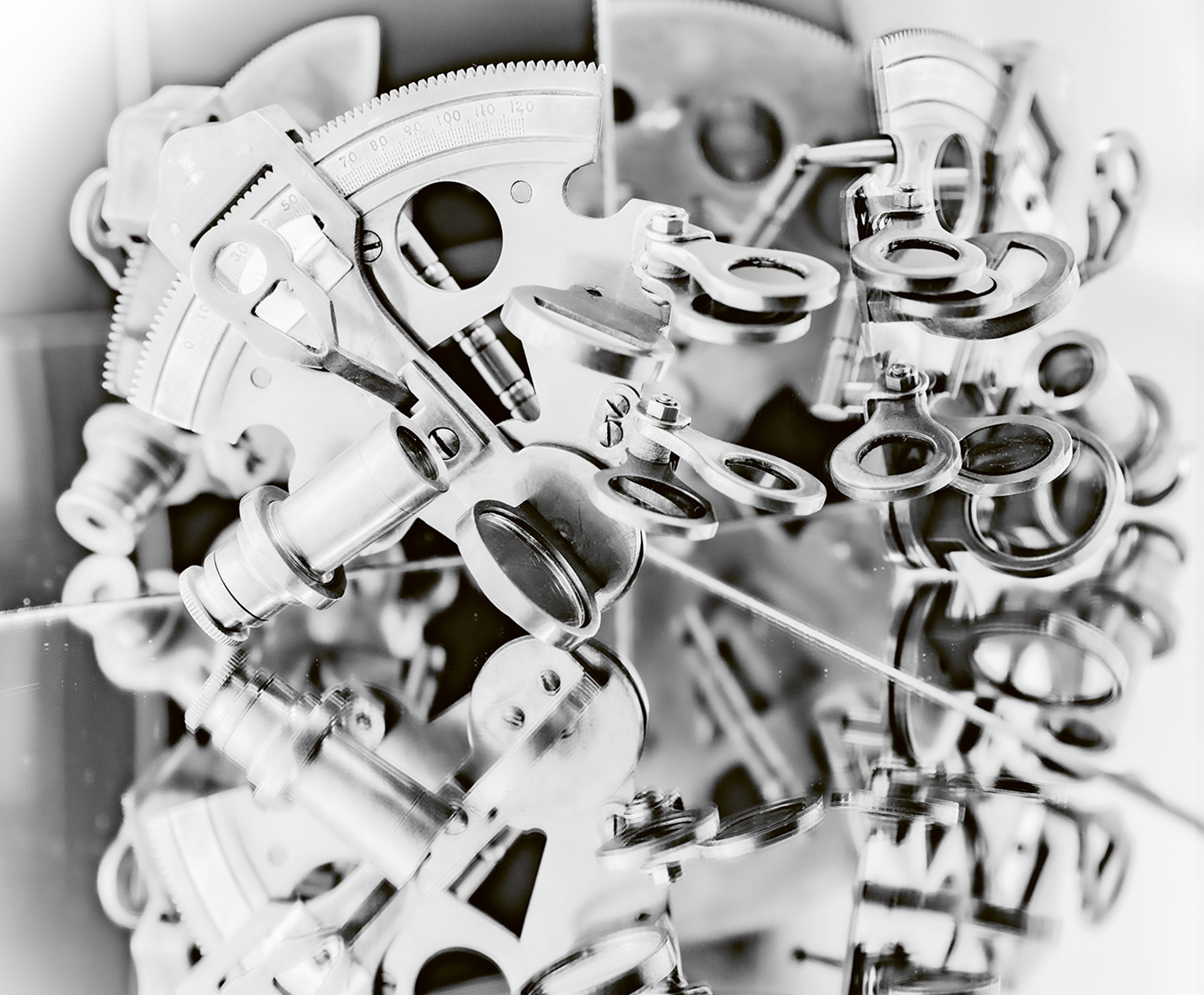 A black and white photographic image showing a sextant - a scientific navigational instrument - which has been placed on top of a mirror so an almost-circular repeating image of the instrument has been created.