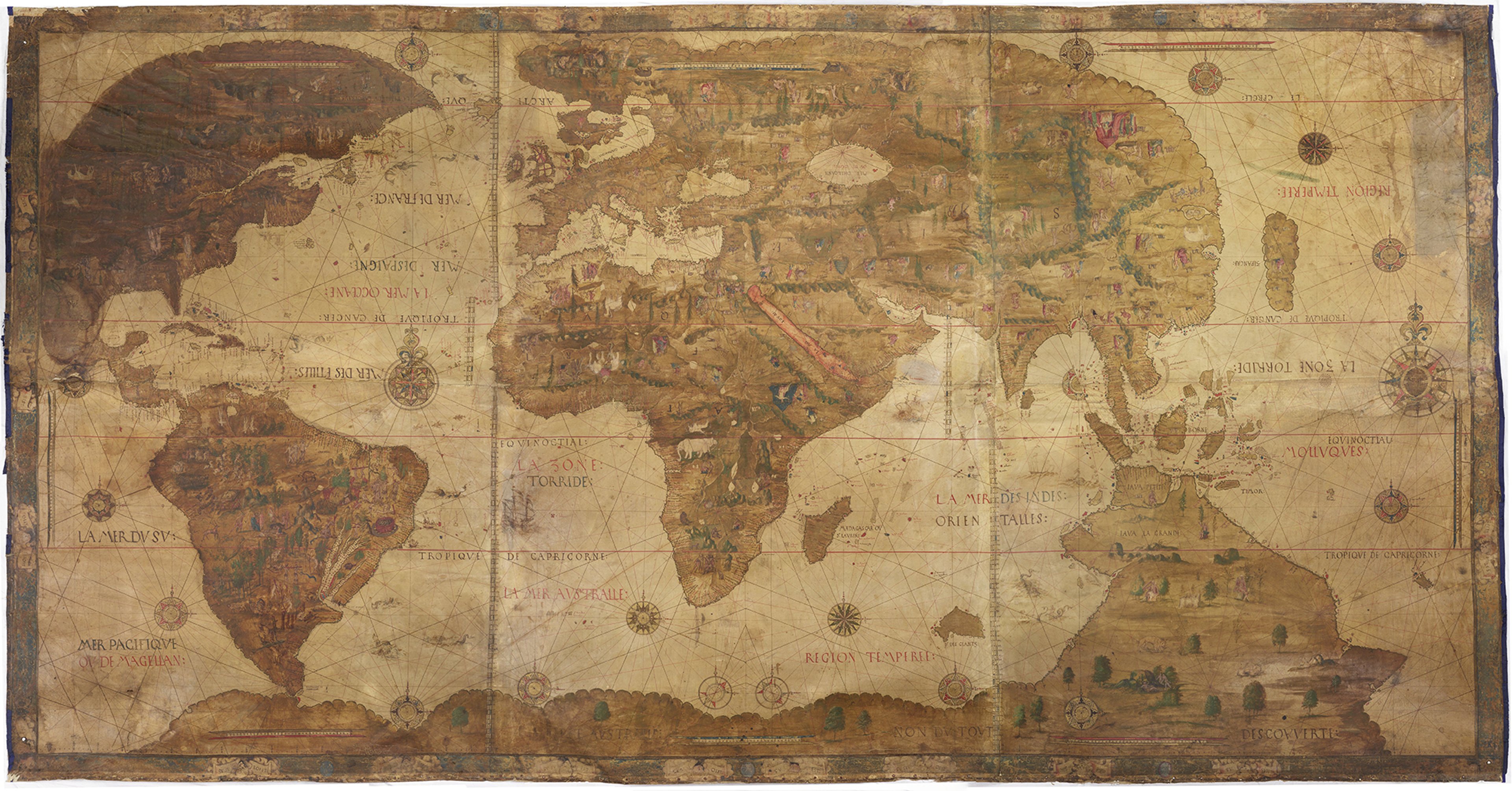 Early world map by Pierre Desceliers. The map is browned with age and shows continents and land in a darker brown/green tone and the oceans in a lighter yellow/brown tone. Across the map, physical geography is highlighted such as trees and mountain ranges. Ships and compass roses features in the oceans.