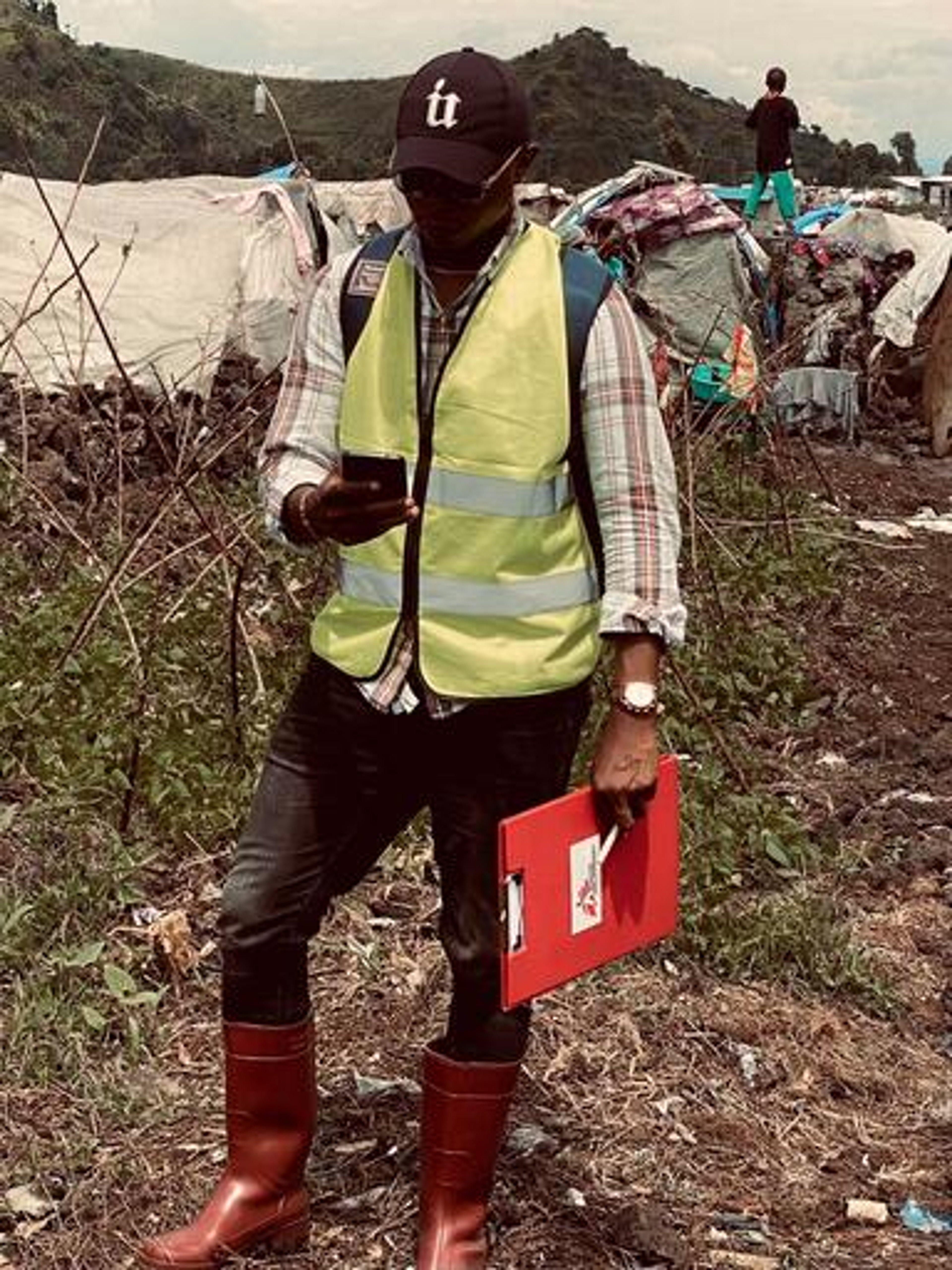 MSF surveyor doing mobile data collection. He holds a bright red clipboard and wears red wellies.
