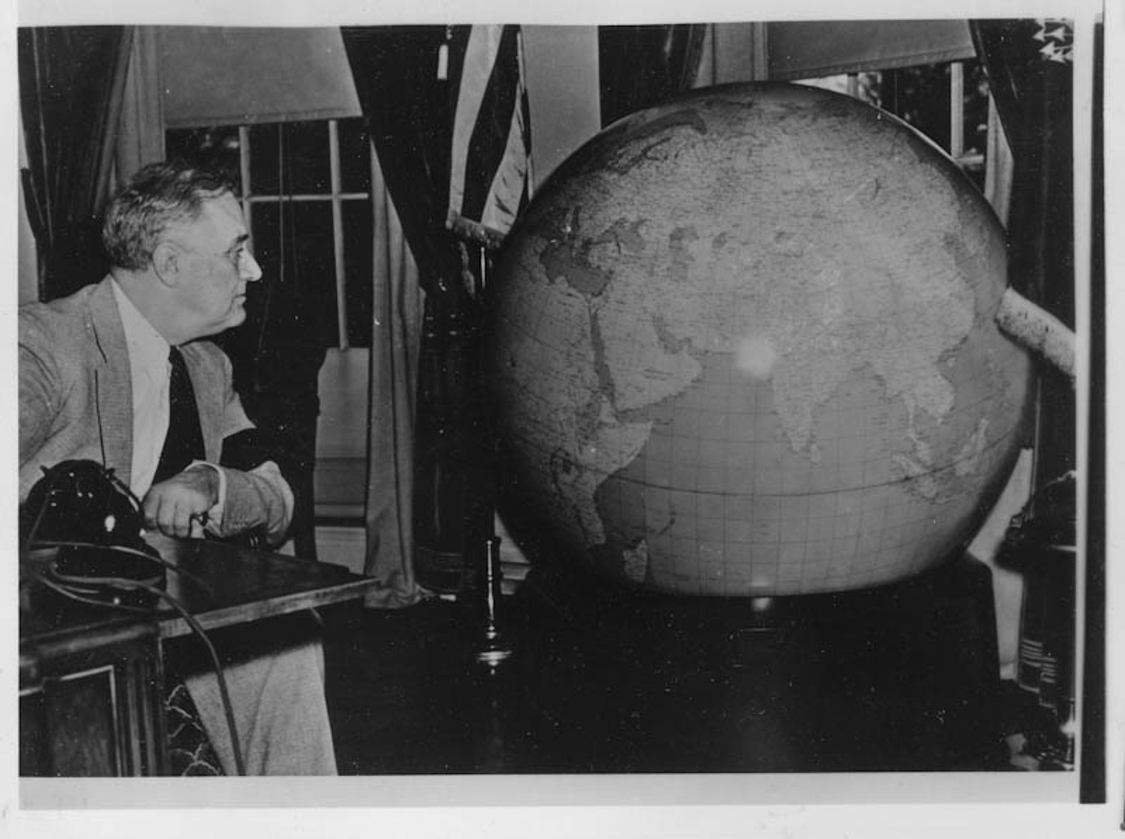 A black and white photograph showing Franklin D. Roosevelt looking at a very large terrestrial globe, presented to him by the United States Army at the White House