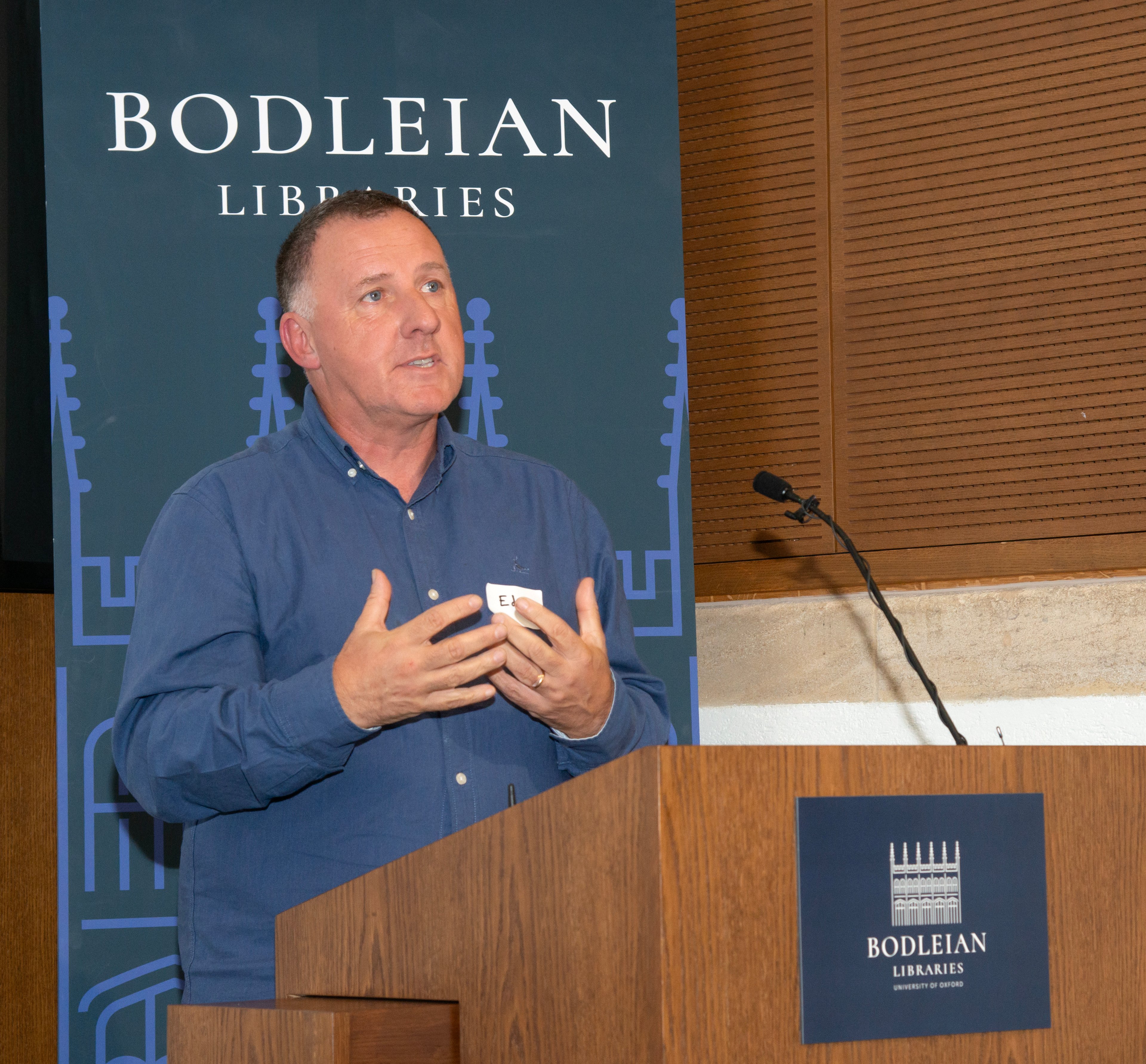 Portrait of Ed Parsons, white male in blue shirt, delivering his keynote speech at Maps Are Too Exiting! The Sunderland Collection Symposium at Bodleian Library