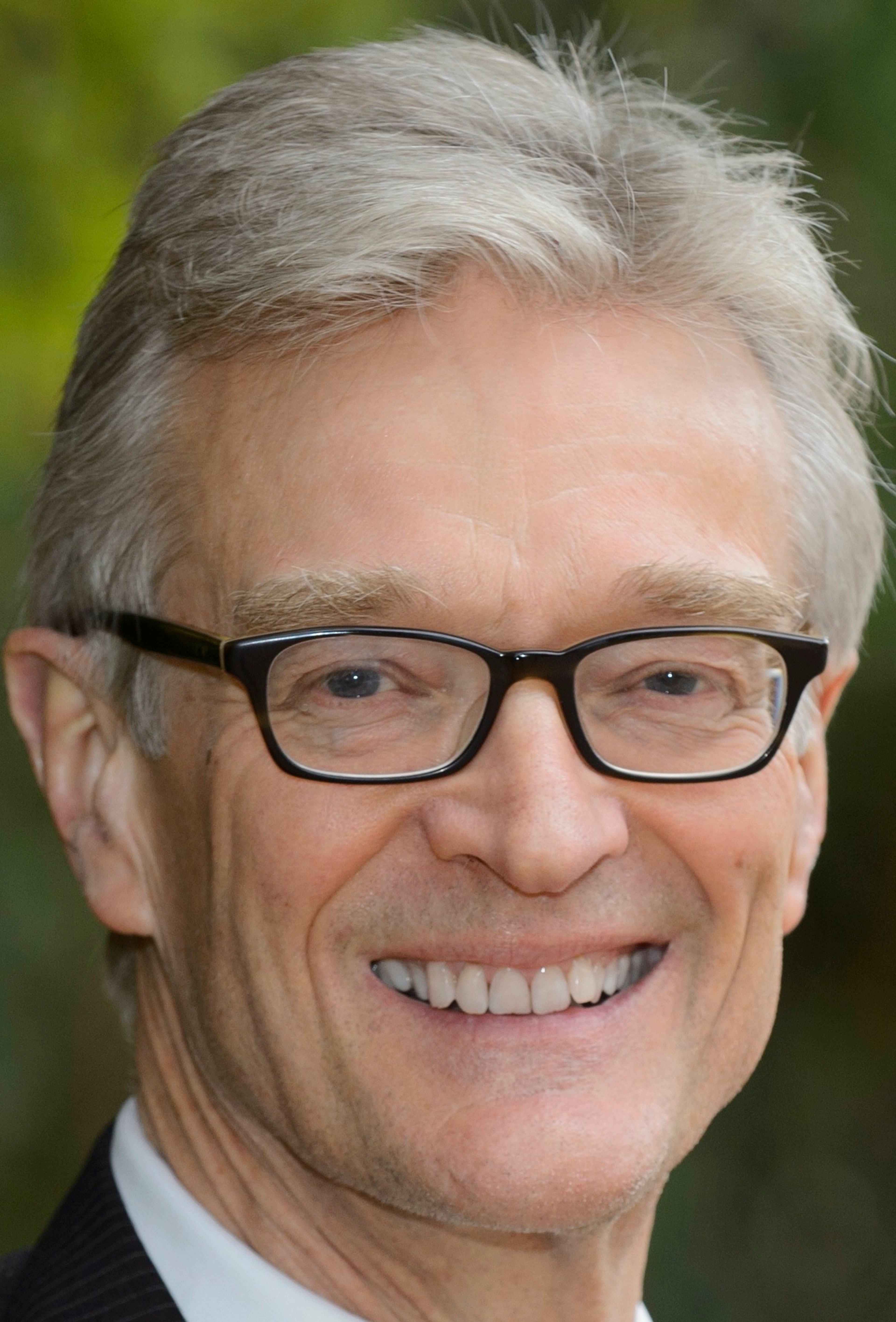 Headshot portrait of Nick Crane, a smiling older white gentleman with black glasses and white hair.