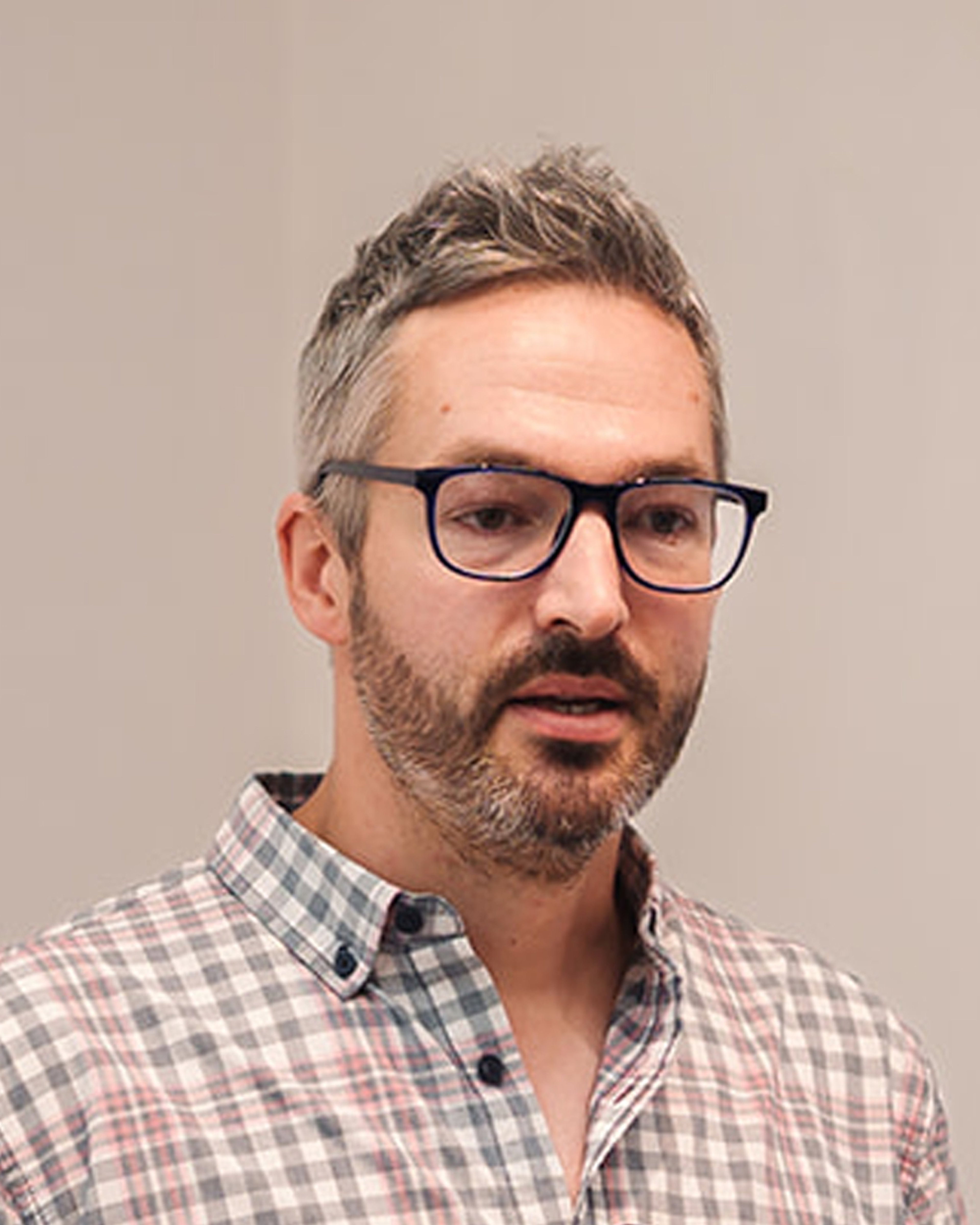 Photograph of explorer Tom Allen, a white man wearing black glasses and a check shirt. He has short hair in a quiff and a beard.