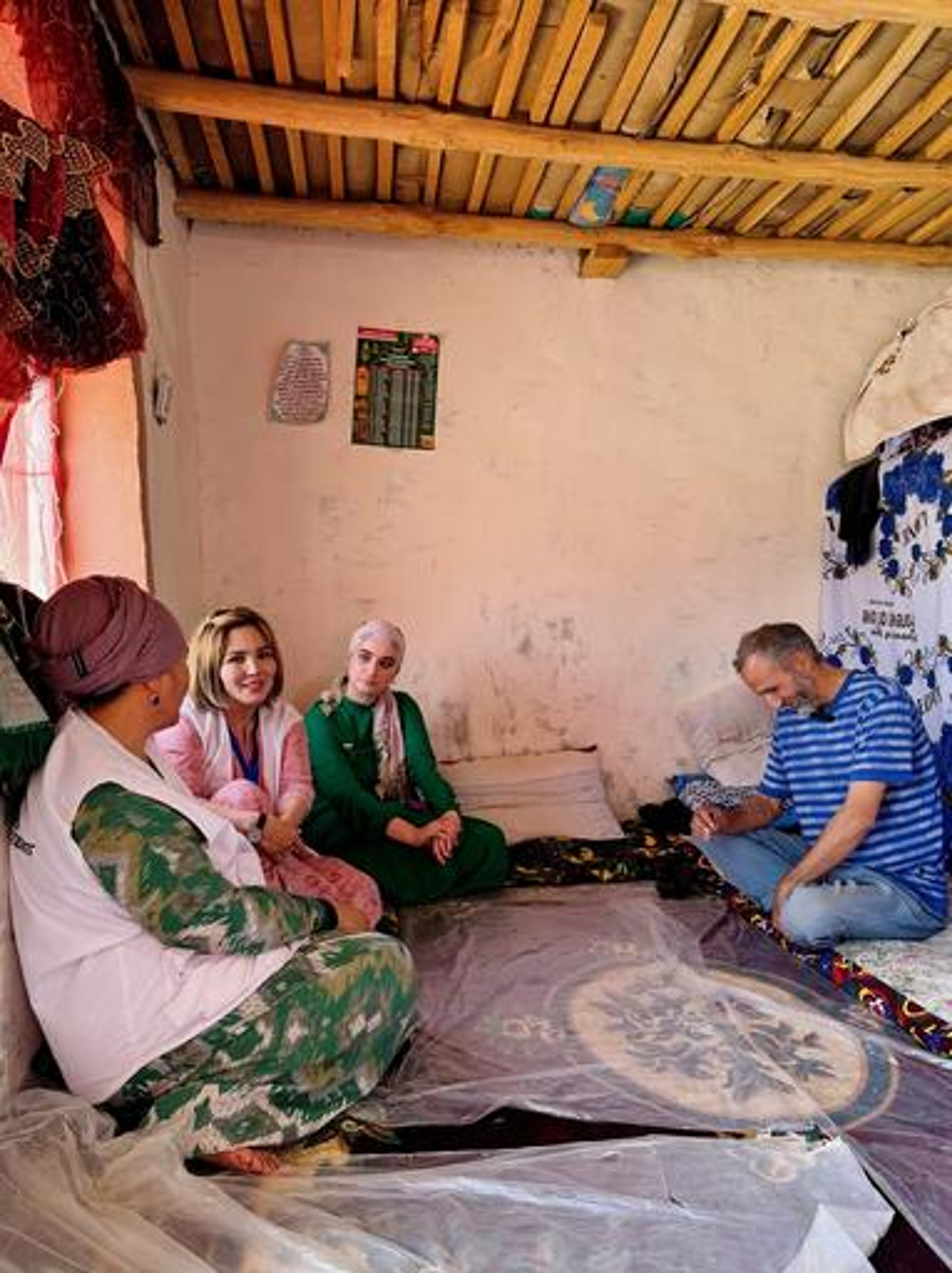 Medics from MSF and a local state hospital in Tajikistan visit Kholnazar Ghairatov, 51, at his home in Kulob district. They are all sat together on the floor and smiling during their conversation. The sun shines through the window.