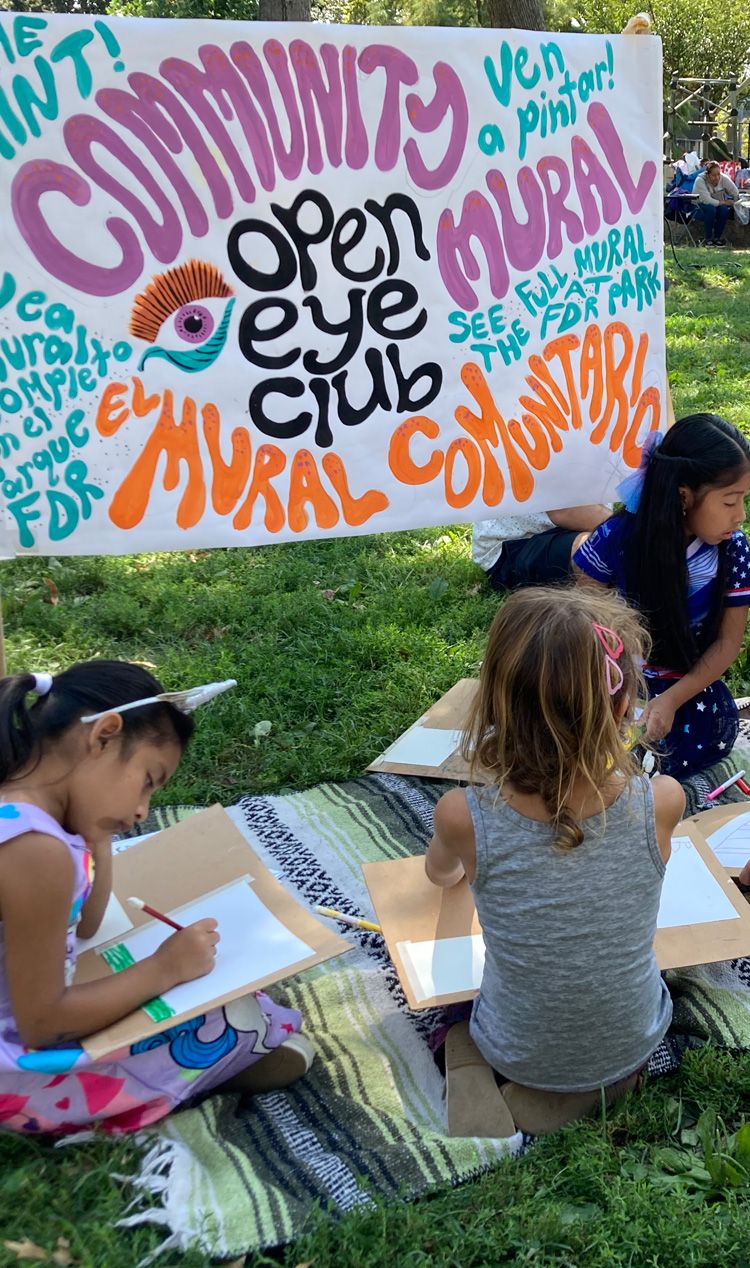 Children drawing in front of an Open Eye Mural Club sign