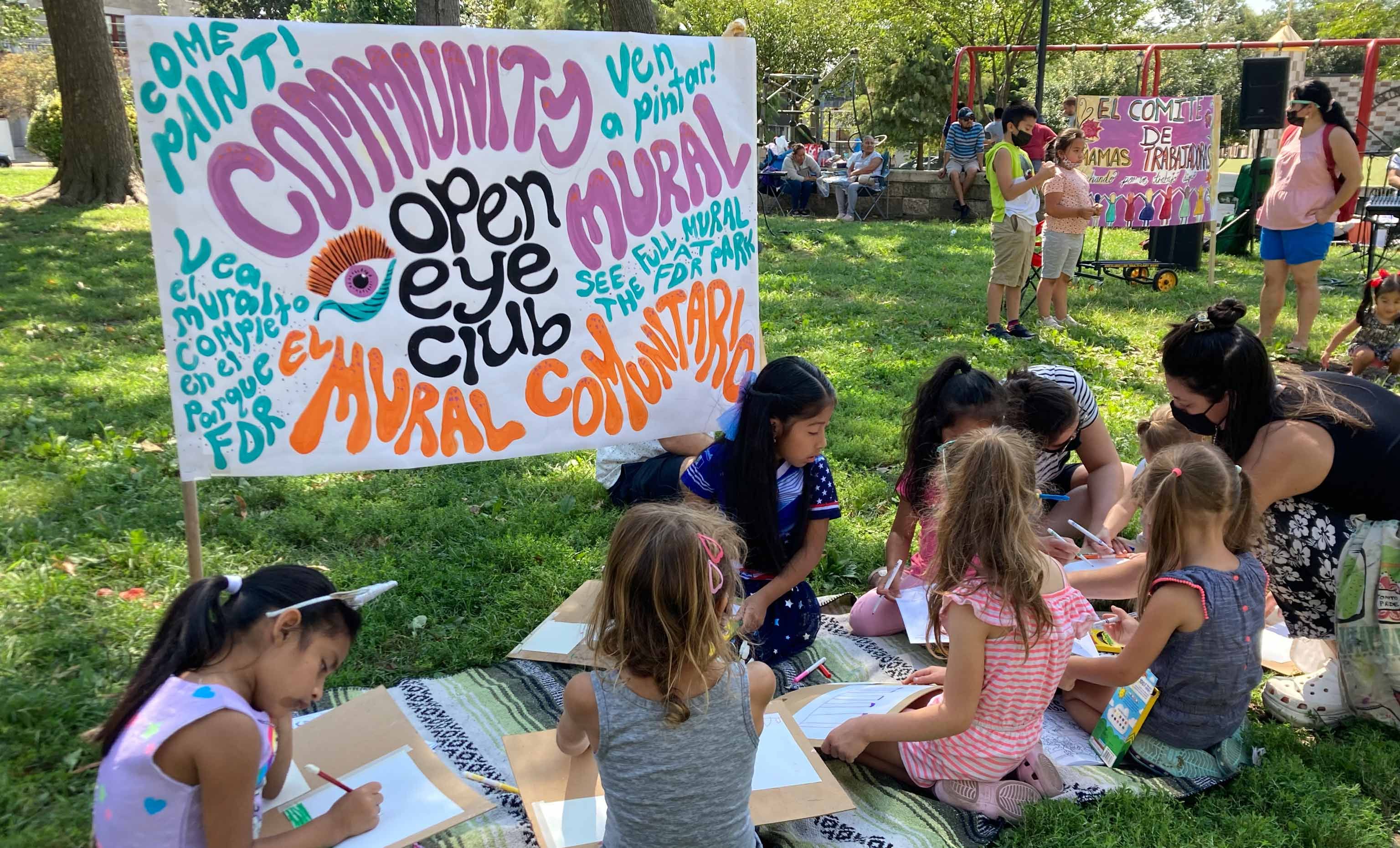 Children drawing in front of an Open Eye Mural Club sign