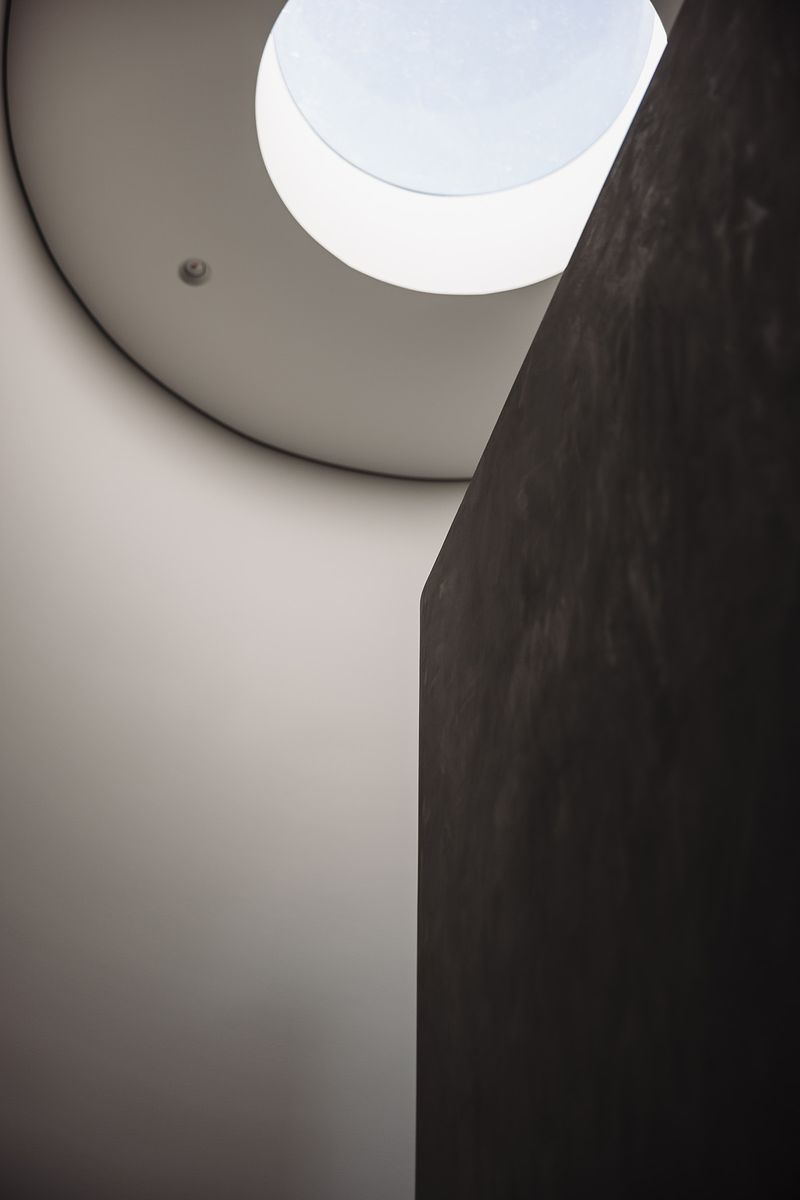 Round skylight above a curved rendered wall