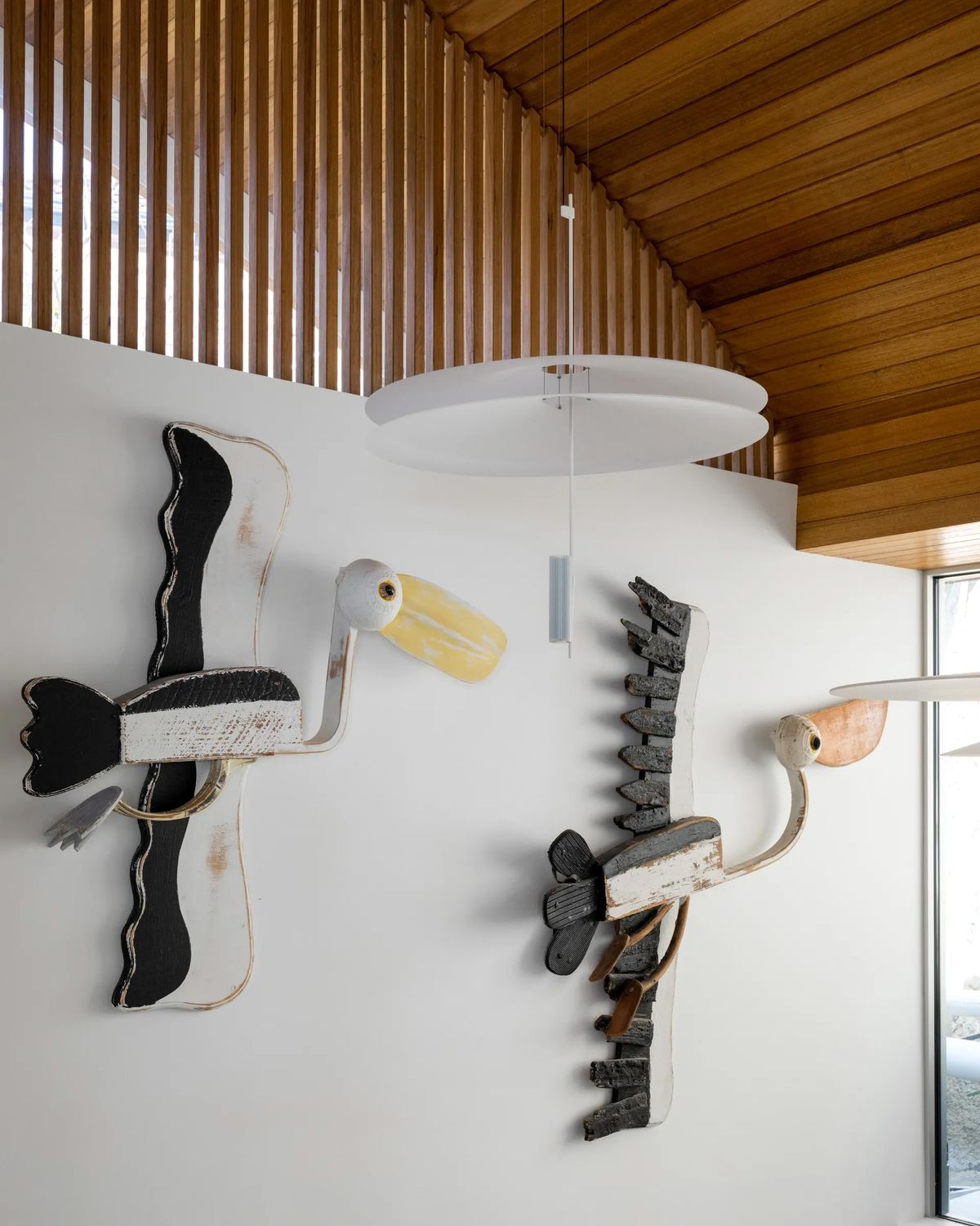 Sculptural bird artworks on a white wall beneath a timber ceiling