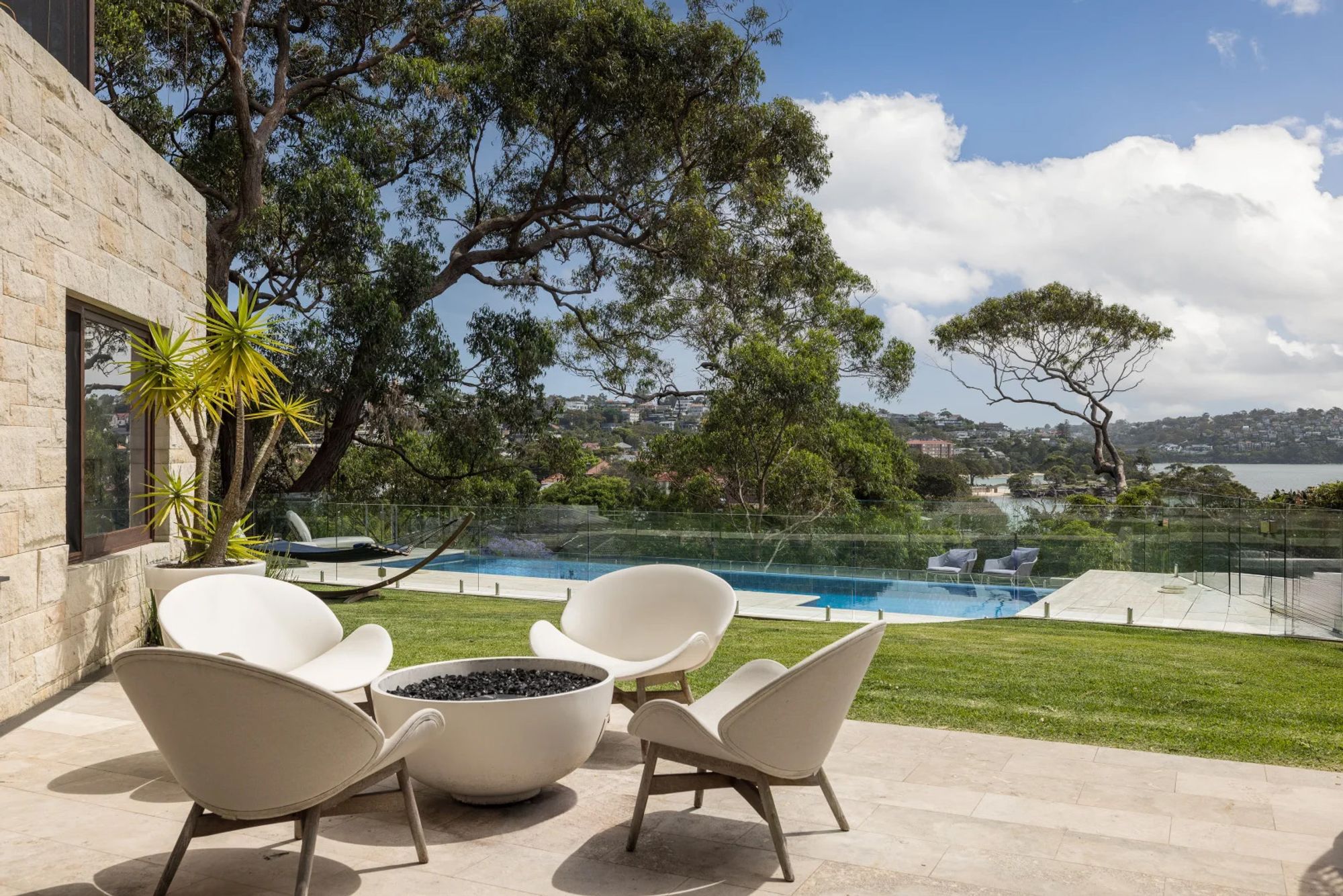 Pool terrace at Quiet House with white lounge chairs beneath a tree, the harbour beyond