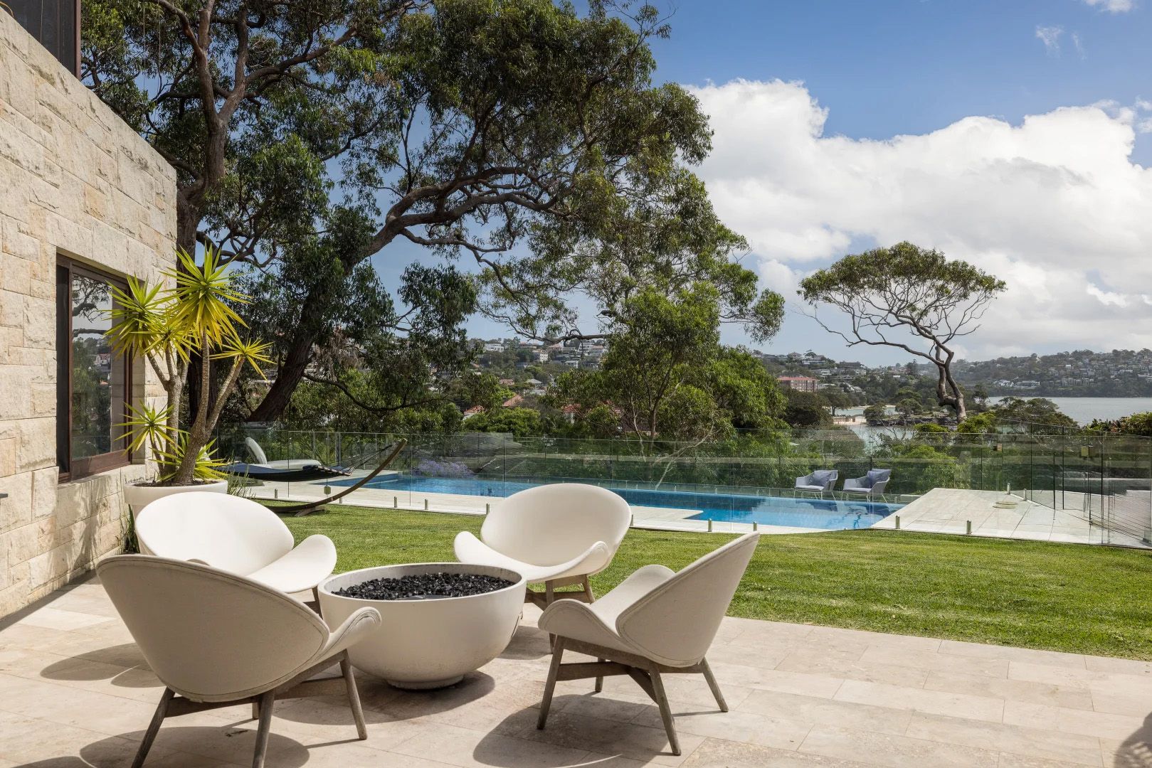 Pool terrace at Quiet House with white lounge chairs beneath a tree, the harbour beyond