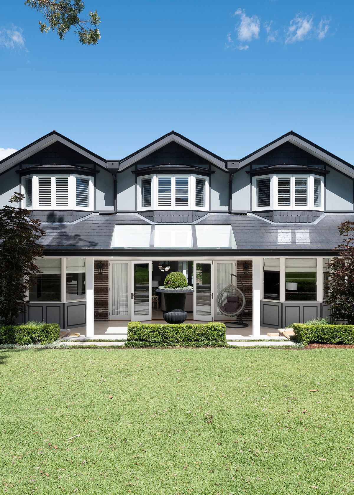 Sussex House rear facade with three gabled dormers above a covered terrace and lawn