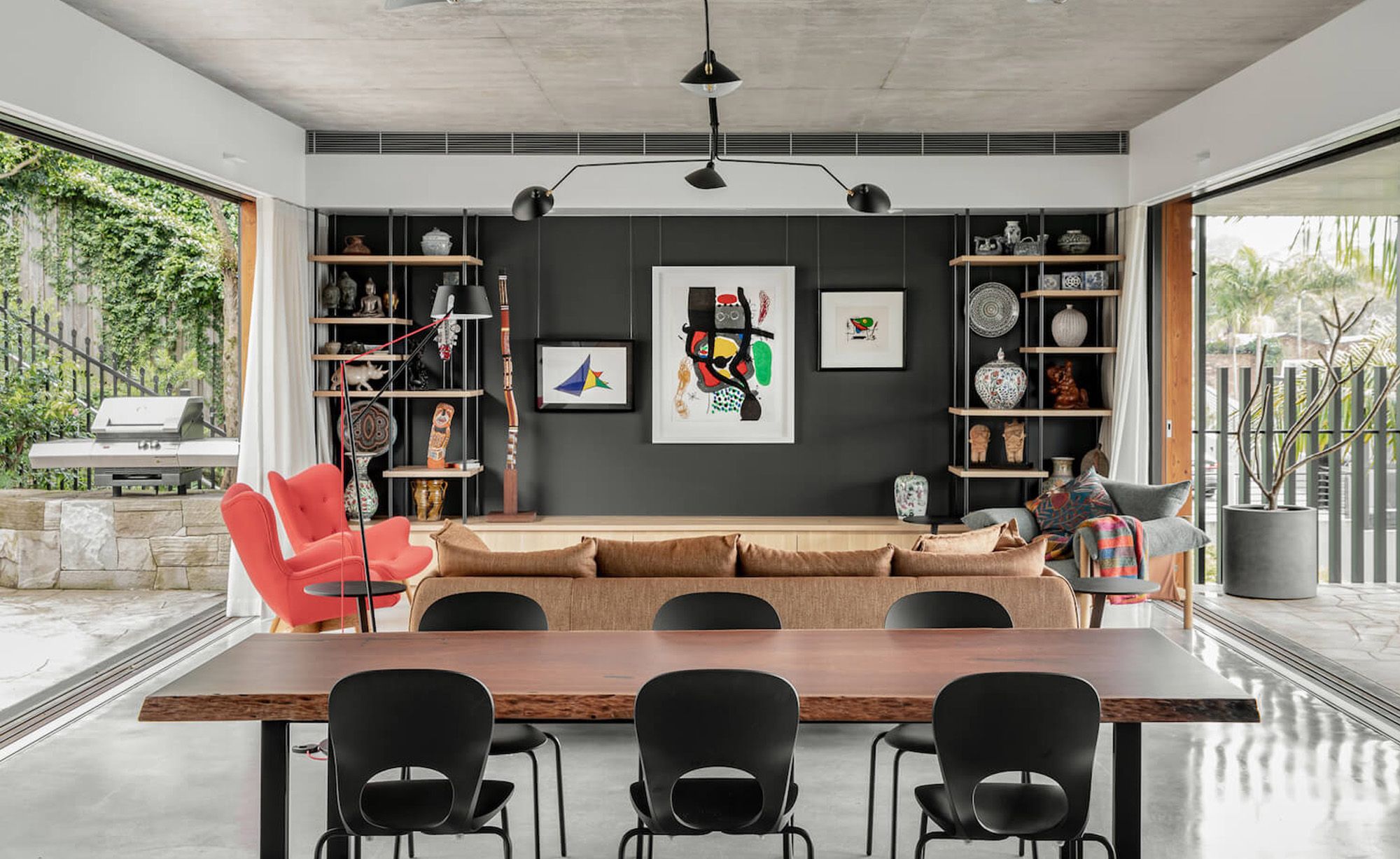 Dining room with a timber table, black shelving and red armchairs, open to the garden